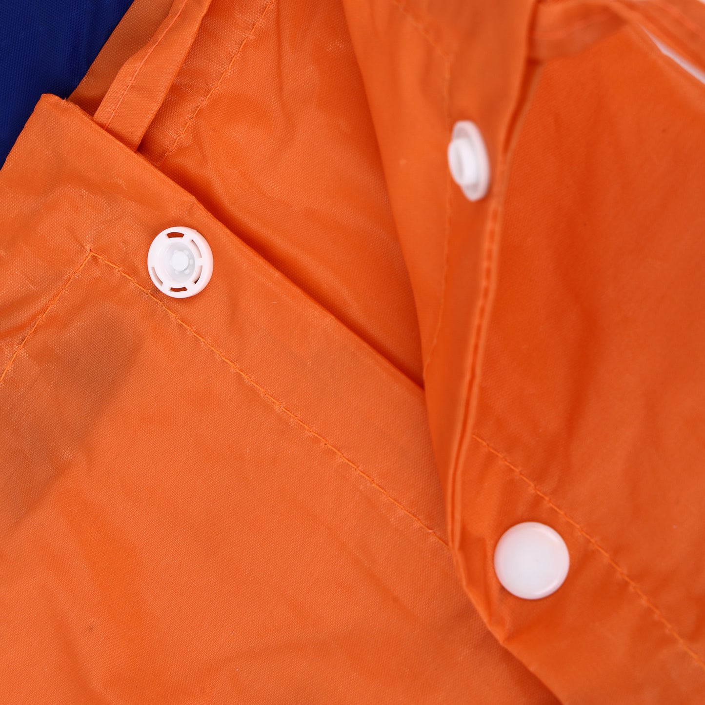 Close-up of an orange waterproof jacket or raincoat showing the fabric texture, white snap buttons, and a blue section of the outer material at the top left corner.