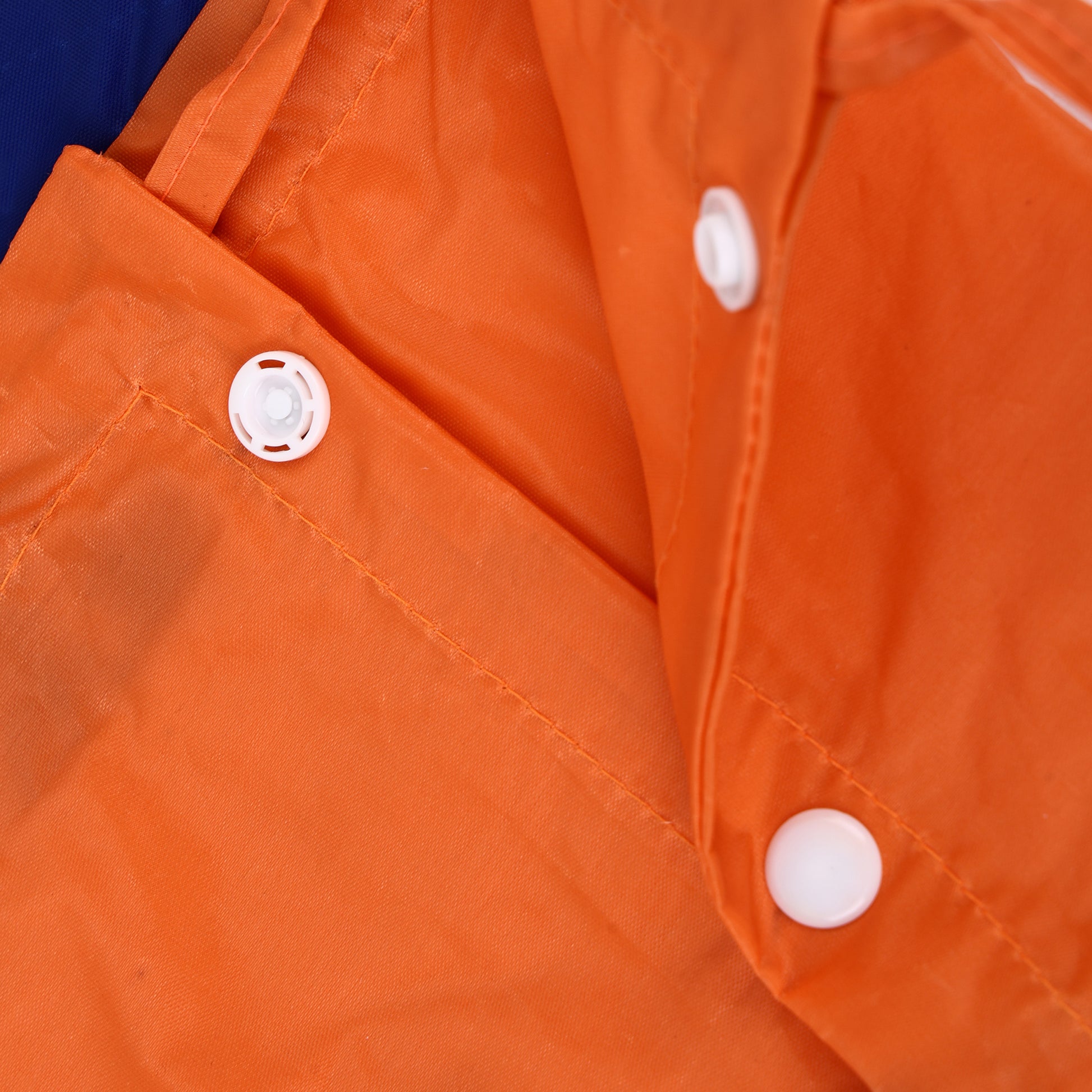 Close-up of an orange waterproof jacket or raincoat showing the fabric texture, white snap buttons, and a blue section of the outer material at the top left corner.