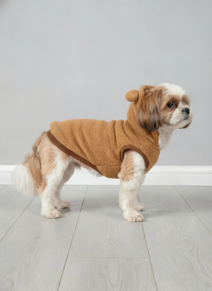 Dog wearing a brown fleece coat with bear ears on a gray floor.