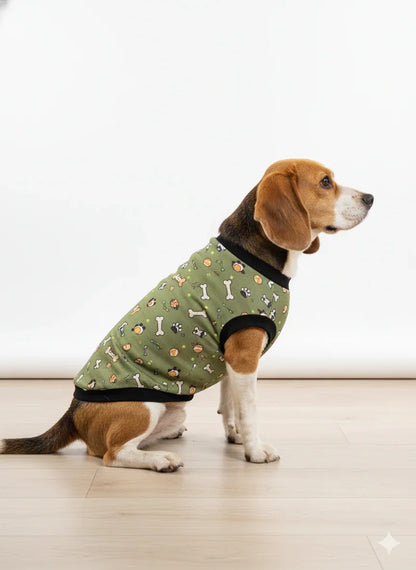 Dog wearing a green patterned coat on a light wooden floor.