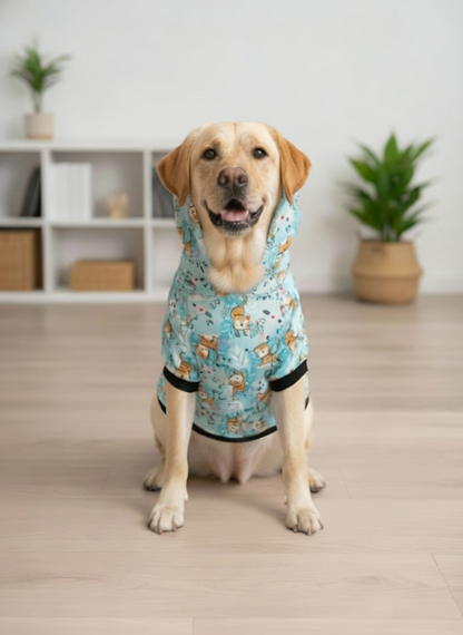 Dog wearing a blue hoodie with cartoon designs indoors on a wooden floor.