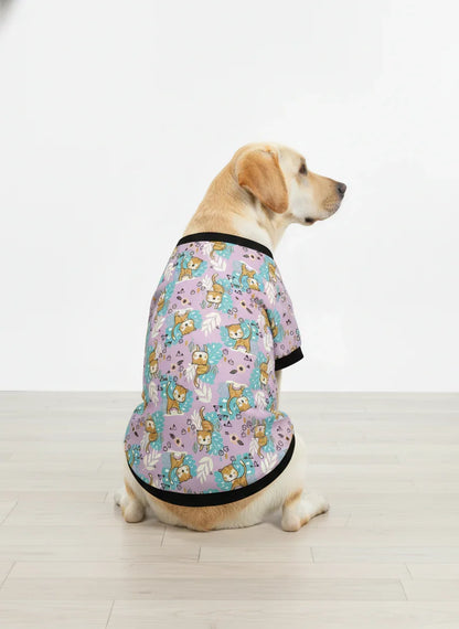 Dog wearing a patterned shirt sitting on a wooden floor.