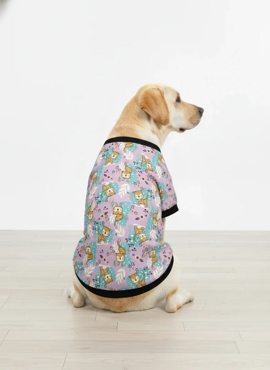 Dog wearing a patterned shirt sitting on a wooden floor.
