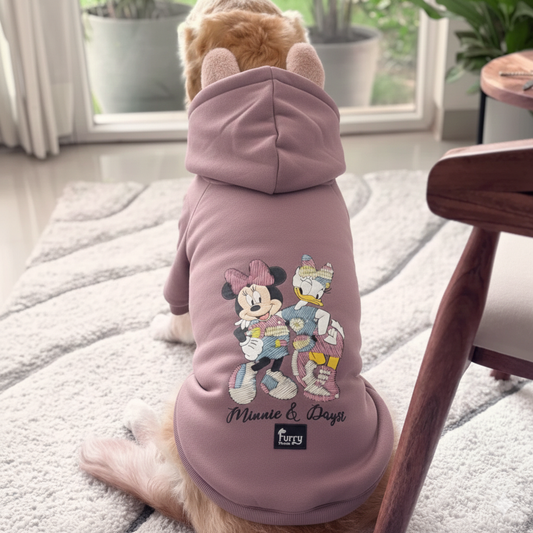 Dog wearing a pink hoodie with cartoon characters on a rug.